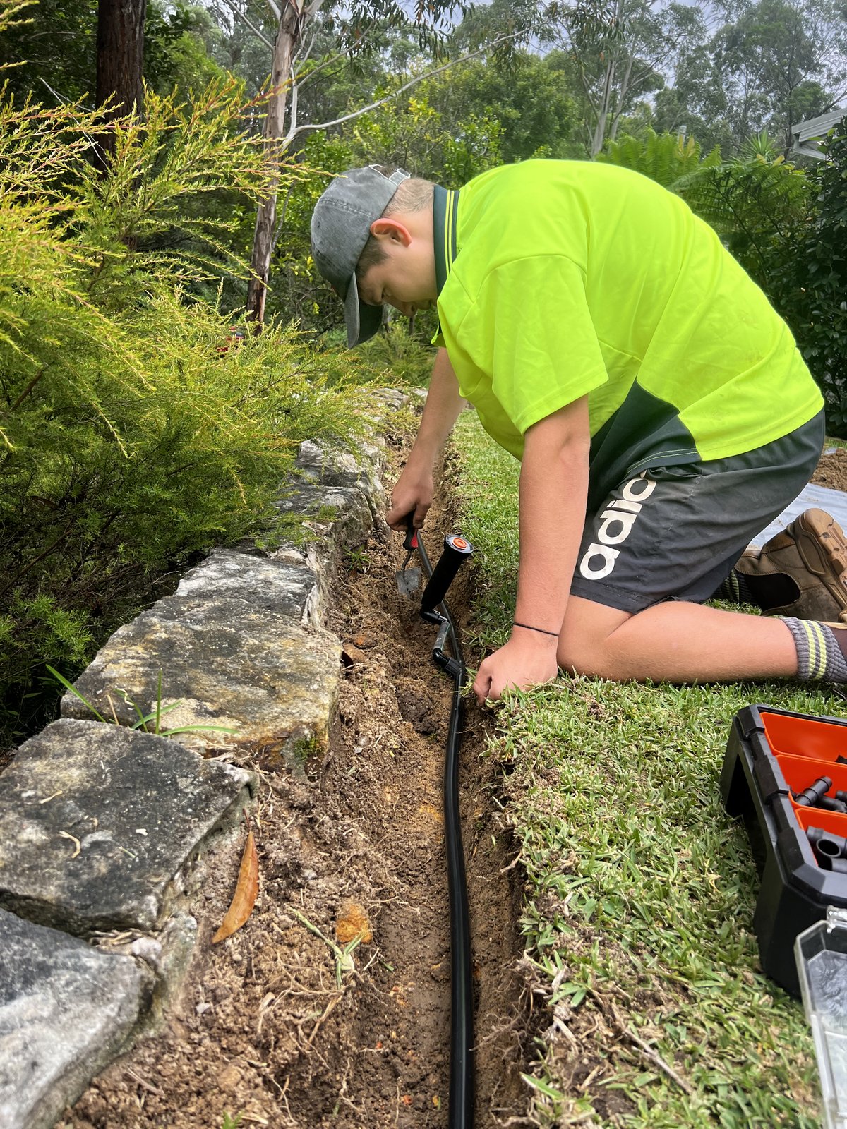 Custom Irrigation Solutions tradesperson installing irrigation in stone-walled garden bed Sydney